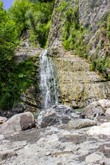 Mountain waterfall. It flows down from the rocks to form a blue lake. There is a lot of greenery around.
