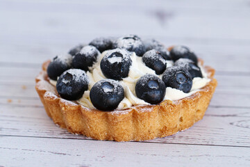 Close-up dough tartlet with creamy white cream and sweet blueberry. On a white background.