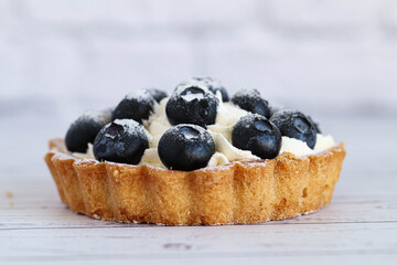 Close-up dough tartlet with creamy white cream and sweet blueberry. On a white background.