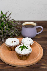 Cupcakes with black currants on a background of flowers and mint leaves, on a round board on a wooden background.