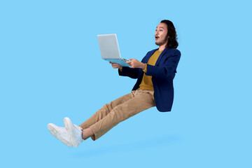 Young asian businessman hand holding computer laptop floating in mid-air isolated on blue background.