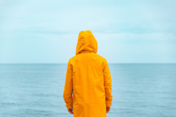woman in yellow raincoat at sea beach cliff at storm rainy weather