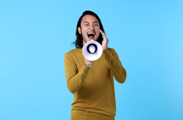 Young Asian man shouting into megaphone isolated on blue background.