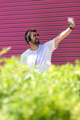 Bearded man with sunglasses taking a selfie against pink wall