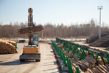 An industrial loader loads logs into a conveyor at a sawmill