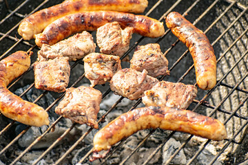 Grilling pig meat and sausages for a campfire party.