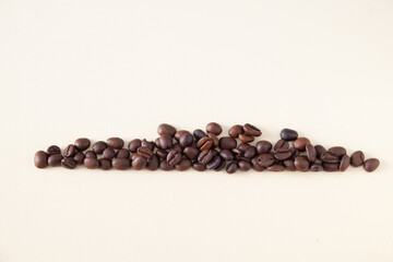 A line of toasted coffee beans against a beige background, the ripple of the top of the beans recall the movement of the waves of the sea.