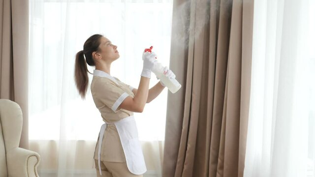 Housemaid spraying air freshener at home or hotel apartment, shot in in slow motion. Cleaning concept. Beautiful maid sprinkling perfume scent from spray bottle. 4 k video