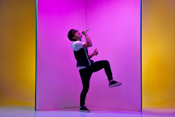 Fototapeta na wymiar Celebrity. Young male musician, singer performing on pink-orange background in neon light. Concept of music, hobby, festival, entertainment, emotions. Joyful party host, singer, portrait of artist.
