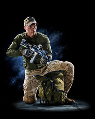 Army soldier in Protective Combat Uniform holding Special Operations Forces Combat Assault Rifle on dark background