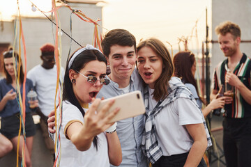 Taking selfie. Group of young people in casual clothes have a party at rooftop together at daytime