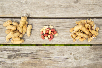 A small pile of peeled ground peanuts next to a small pile of unpeeled peanuts and peanut skins on a wooden table. View from above.