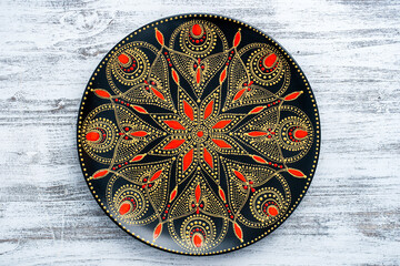 Decorative ceramic plate with black, red and golden colors, painted plate on the white wooden...