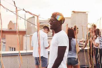 African american man smiling and dancing. Group of young people in casual clothes have a party at rooftop together at daytime