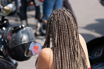 girl with a hairstyle with many African braids standing in an embrace among many motorcyclists,...