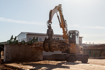 An industrial loader loads logs into a conveyor at a sawmill