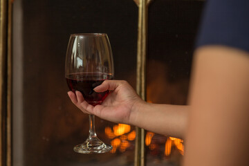 hand holding a large wine glass as background a burning fireplace, part of the arm is shown