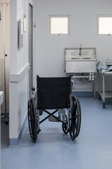 Fototapeta na wymiar black wheelchair in a hospital, metal sink background, doors and windows and blue floor
