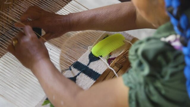A woman hand weaving a tapestry on a loom in Oaxaca, Mexico. Over the shoulder shot of her hands. Close-up, slow-motion.