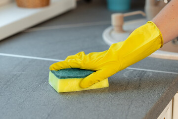 Woman's hands in yellow gloves cleaning counter top in kitchen