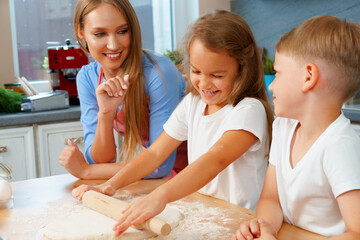 Mother and her little kids, boy and girl, helping her to prepare dough