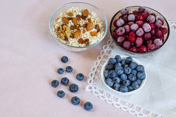 Bowl of oatmeal for porridge with ingredients of almond nuts and raisins on beige linen background. Fresh blueberry, frozen cherry. Every day healthy breakfast. Diet food. Flat lay