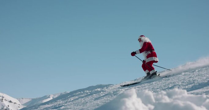 Old man in red Santa Clause costume with beard skiing in mountains. Santa relaxing in winter resort, carving turns on piste - christmas, winter sports concept 4k footage
