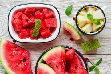 Sliced watermelon, melon cubes in a cup and mint leafs on vintage wood table.
