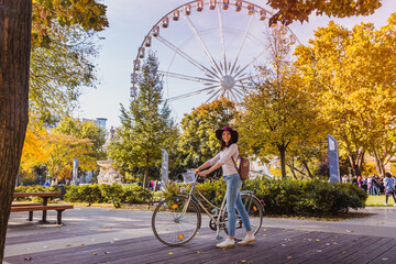 A happy young woman travel by bicycle and stop near the Budapest Eye big Ferris wheel in Budapest
