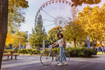 Foto auf Acrylglas Eine glückliche junge Frau fährt mit dem Fahrrad und hält in der Nähe des großen Riesenrads Budapest Eye in Budapest © Evgeniya Biriukova