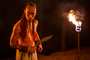 Irdorath group, clip making backstage. The caucasian man with dreadlocks, with knife in the hand. Viking's nighttime in the forest is lighting by flamed torches.
