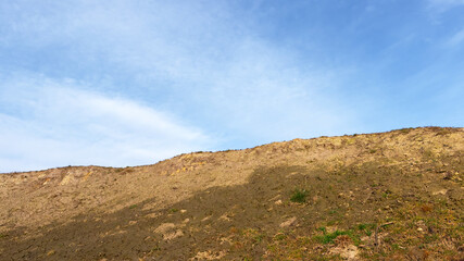 The slope of a clay hill against the backdrop of a beautiful blue sky. Lifeless soil. Sunny weather. Landscape.