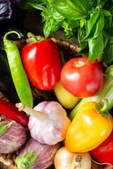 Various vegetables in a basket on a brown wooden table. Lots of raw vegetables in the basket. Eggplant, tomatoes, garlic, sweet peppers, onions on the table. Top view with space for text. Healthy food