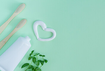 Bamboo toothbrushes, white tube of toothpaste, mint leaves on light green background. Heart shape...