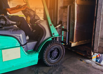 Fototapeta na wymiar Worker driving forklift loading and unloading shipment carton boxes and goods on wooden pallet from container truck to warehouse cargo storage in logistics and transportation industrial 