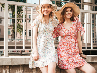 Two young beautiful smiling hipster girls in trendy summer sundress.Sexy carefree women posing on the street background in hats. Positive models having fun and hugging