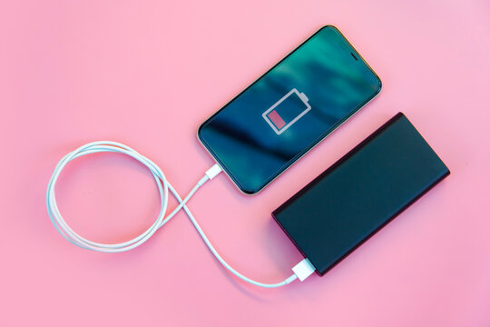 Smartphone charging with power bank on pink background. Flat lay