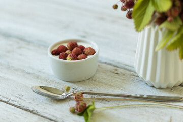Ripe and green strawberries with leaves and flowers in a ceramic vase on a white background. Dessert with cream and berries in a white bowl. Light snack