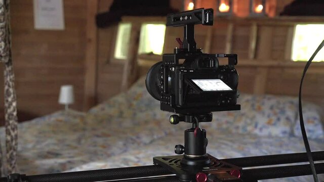 Tracking shot of a slider camera slowly moving on a rack and shooting a video of a large wooden rustical bedroom with a big bed covered with old-fashioned bedsheets. Slider camera shooting a bedroom.