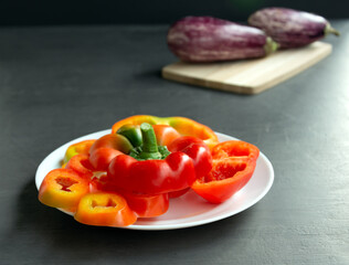 Colorful red peppers on a white plate.Gray background. eggplant on a wooden board