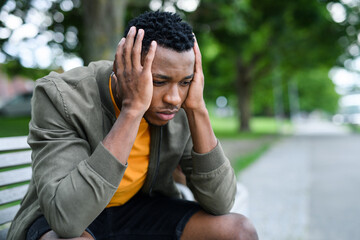 Frustrated young black man sitting on bench outdoors in city, black lives matter concept.