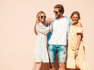 Obraz premium Group of young three stylish friends posing in the street. Fashion man and two cute girls dressed in casual summer clothes. Smiling models having fun in sunglasses.Cheerful women and guy going crazy