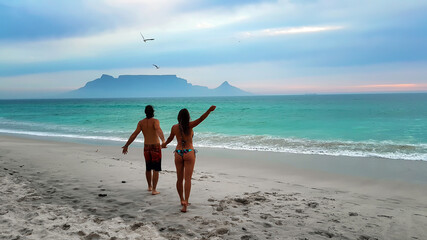 Fototapeta premium Young couple strolling on Cape Town beaches: Bloubergstrand and the view from Table Mountain