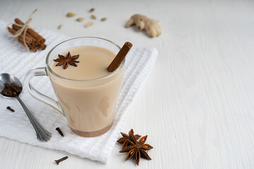 Hot Indian Masala chai or mixed spice tea usually made by brewing black tea with variety of aromatic herb such as anise, cinnamon, ginger and milk on white wooden background. Image with copy space
