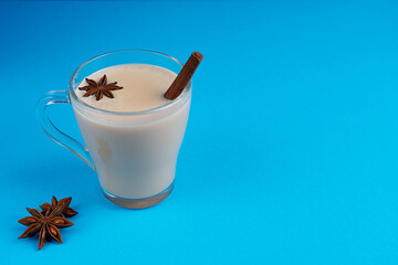 Hot indian masala chai or mixed spice tea made of milk and various spices such as anise and cinnamon in glass cup in a trendy fashion on clean blue background. Image with copy space