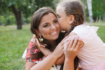 Close up of a happy beautiful woman laughing while her daughter kissing her on a cheek outdoors