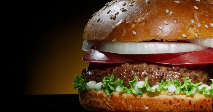 Delicious juicy burger rotating. Yummy hamburger with fresh onions, tomatoes, iceberg cabbage and grilled steak. Tasty pub grub close up shot 4k footage