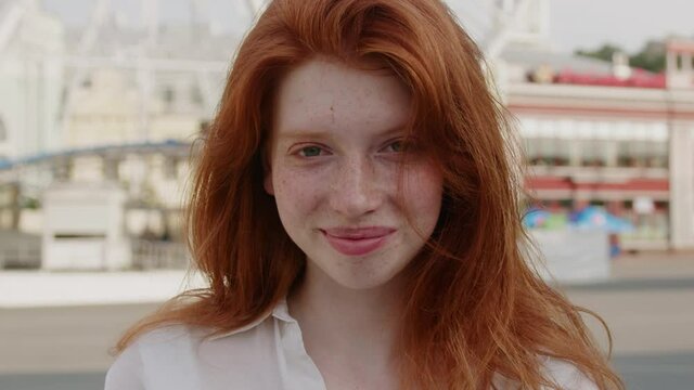 Happy face young sunshine woman with red hair look at camera smile stand in the city streets freckles summer beautiful lady portrait outdoor slow motion