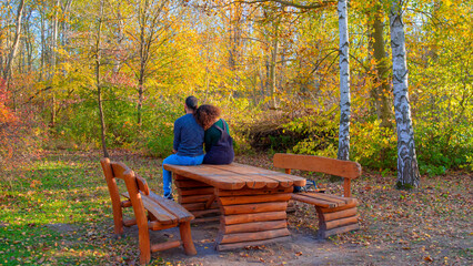 A couple is sitting on the wooden old table in the autumn forest