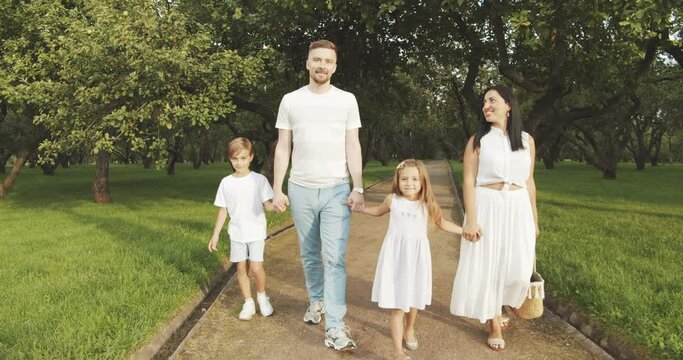 Portrait of a happy family with children holding hands and walking in a picturesque green garden on a sunny day